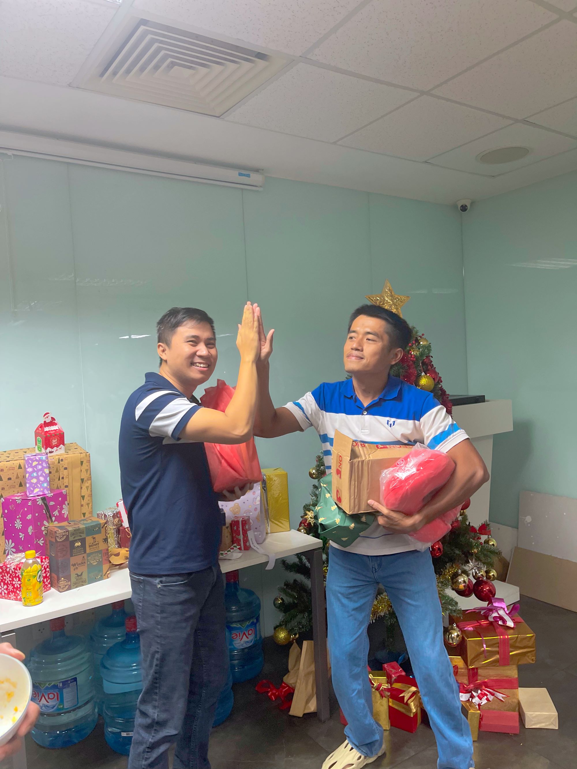 Two men exchanging holiday gifts and high-fiving next to Christmas tree