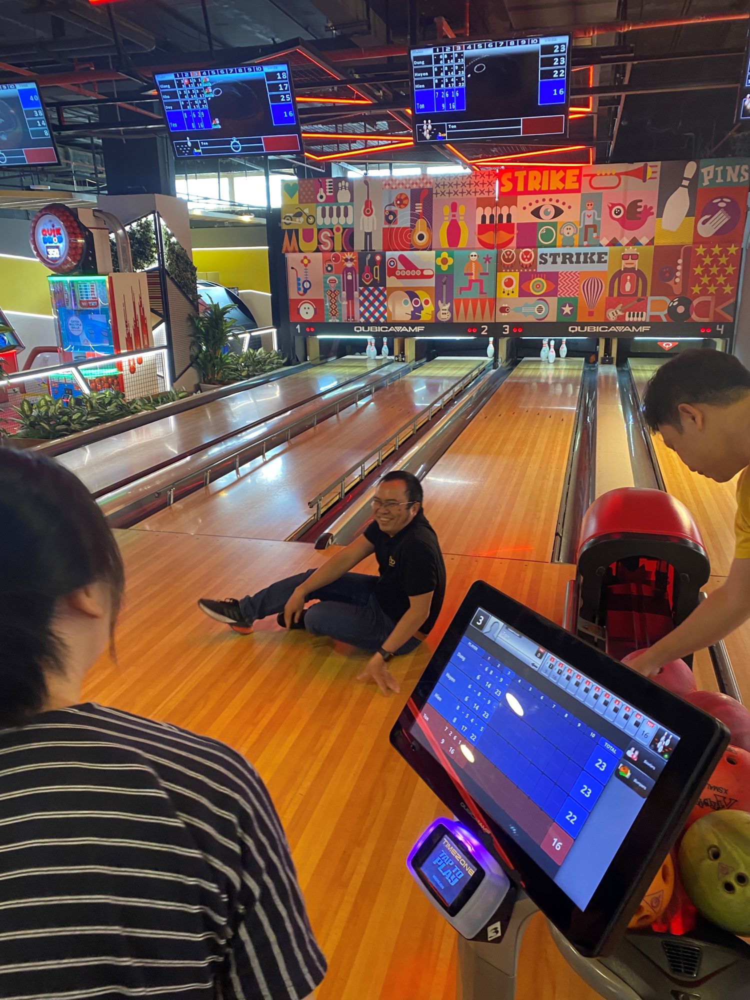Man sitting on bowling alley lane after a strike with scoreboards showing scores