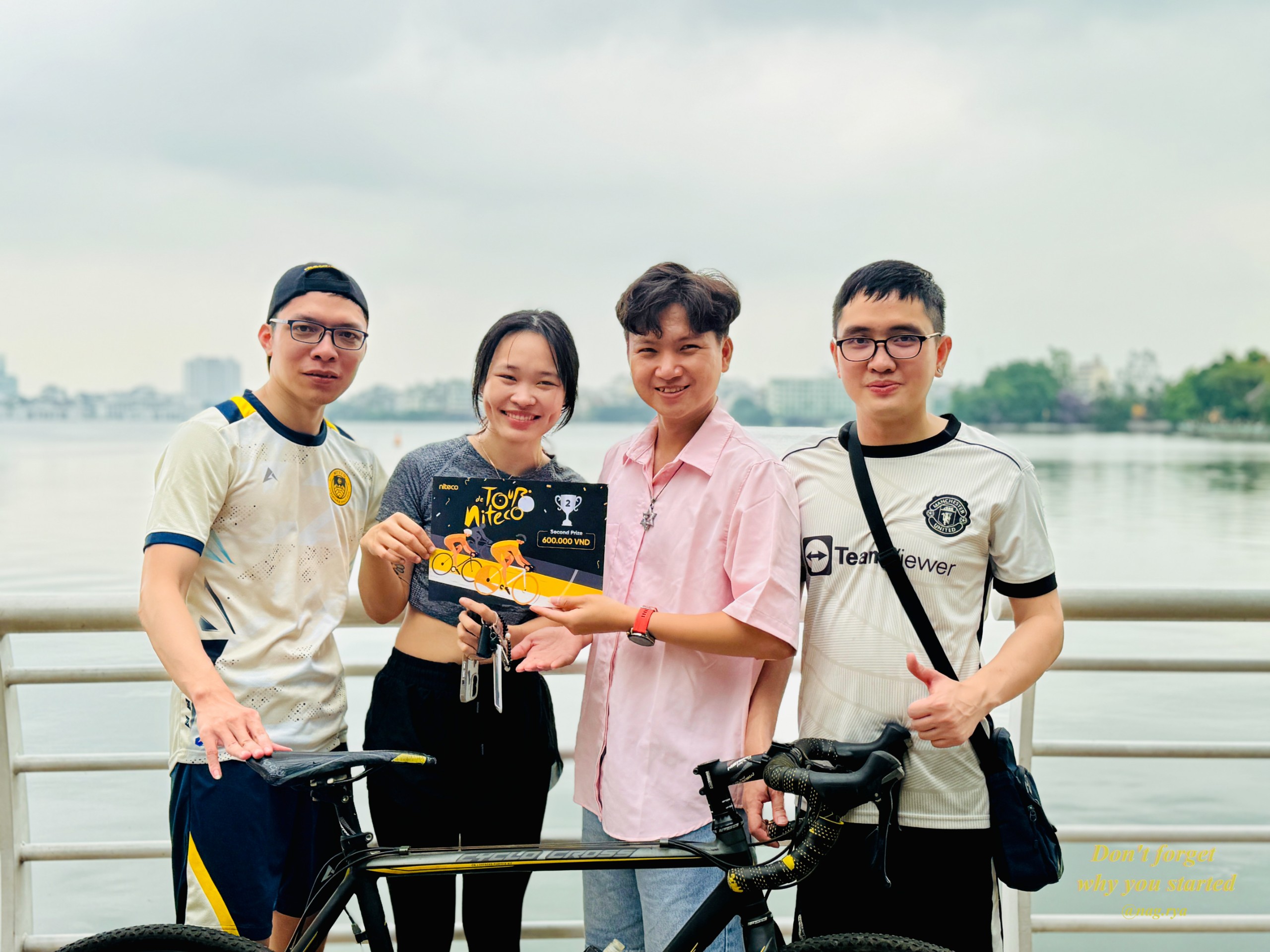 Four cyclists celebrating Tour Niteco race with second prize and bicycle by the lake