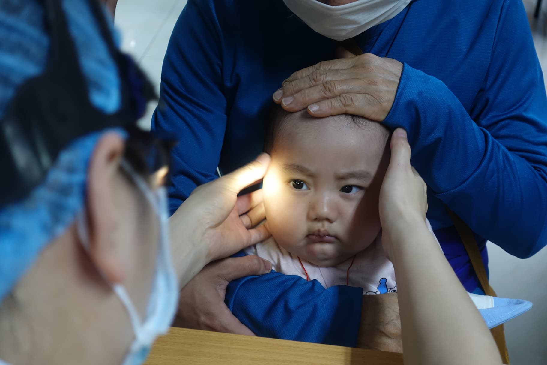 Toddler undergoing pediatric exam with doctor checking ears and head health