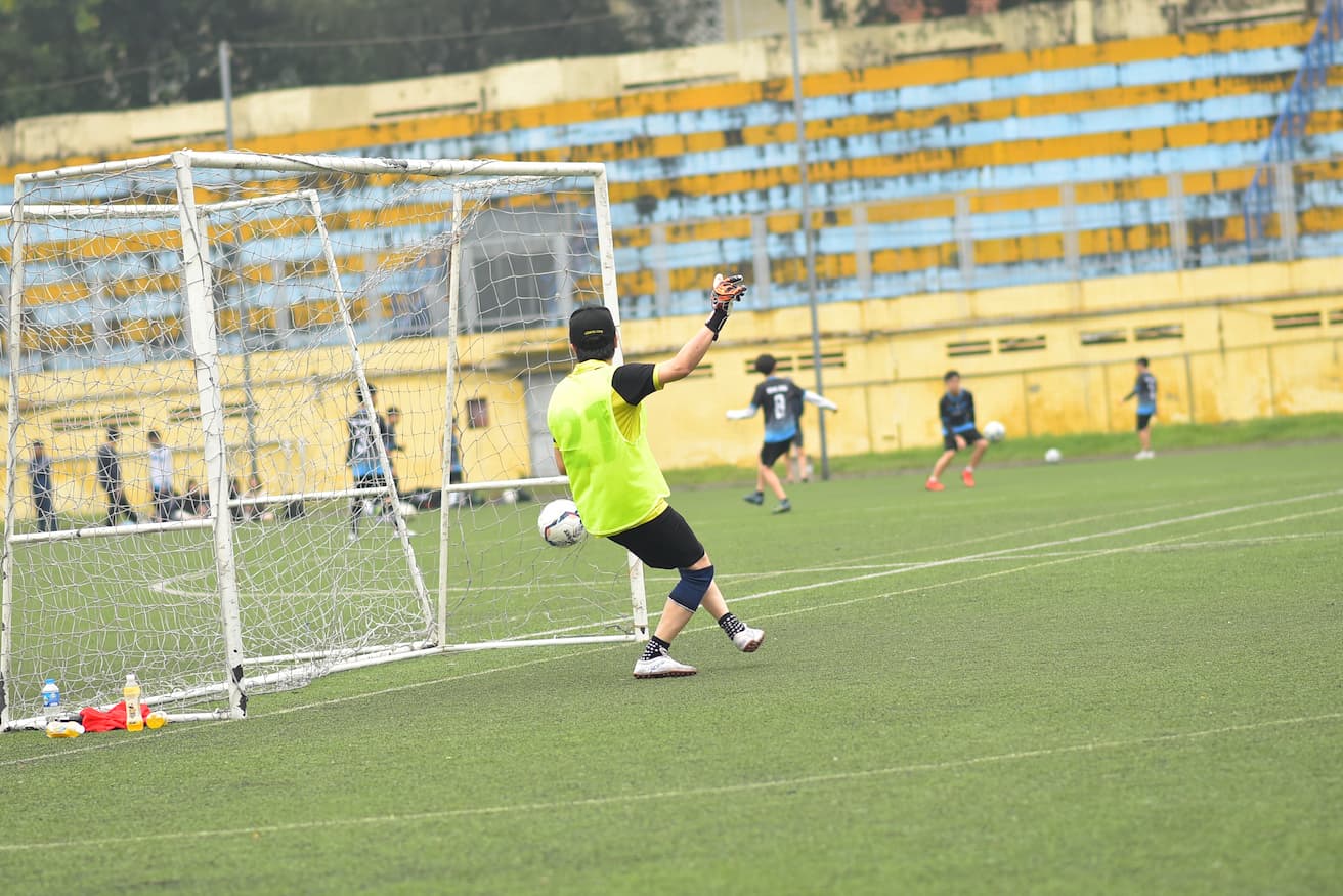 Goalkeeper in neon vest saving a soccer ball during football training session.