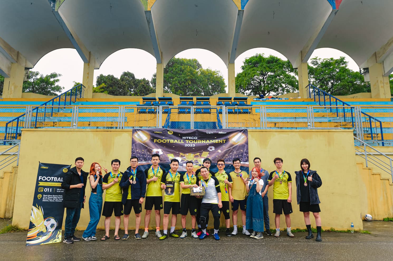Niteco football tournament 2023 team posing with medals and trophy under arches
