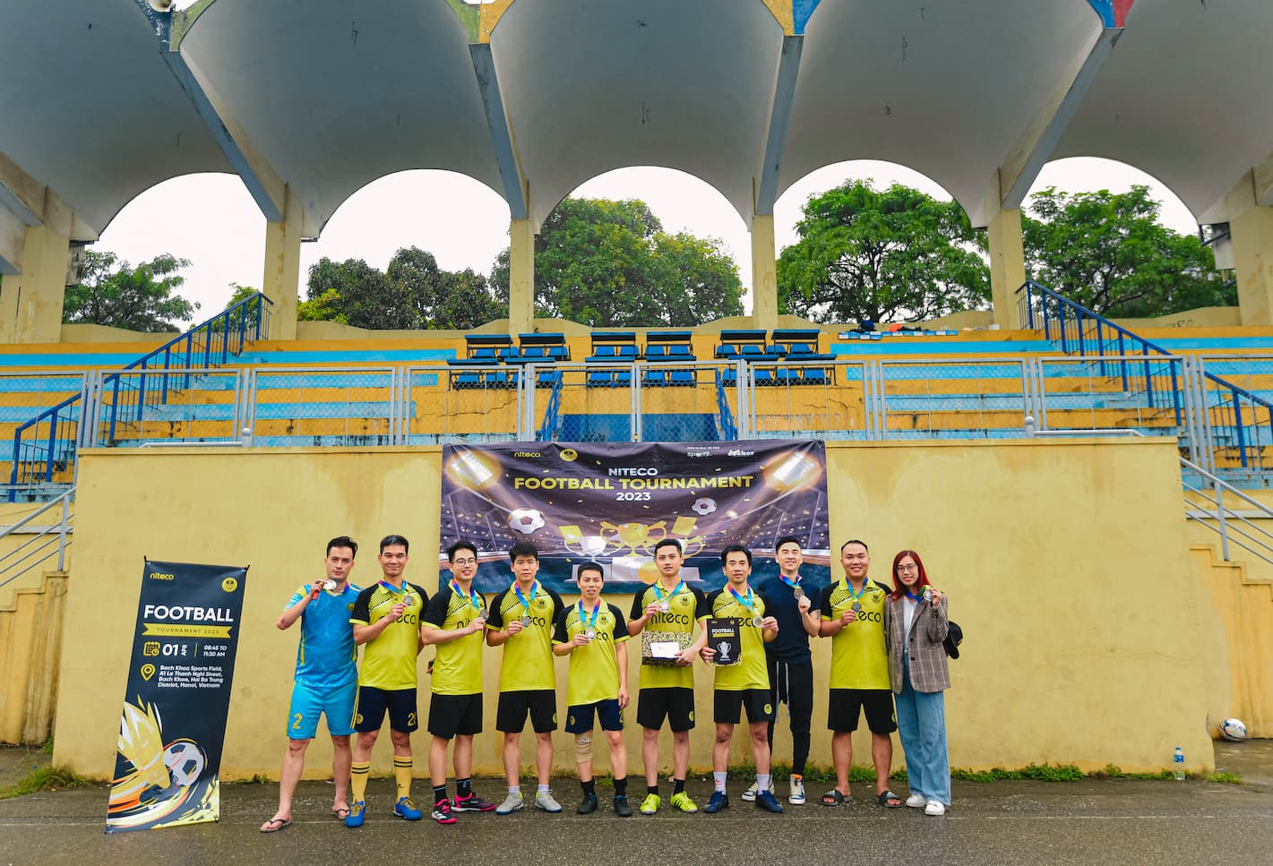 Football tournament 2023 team posing with medals and trophy at sports field stands