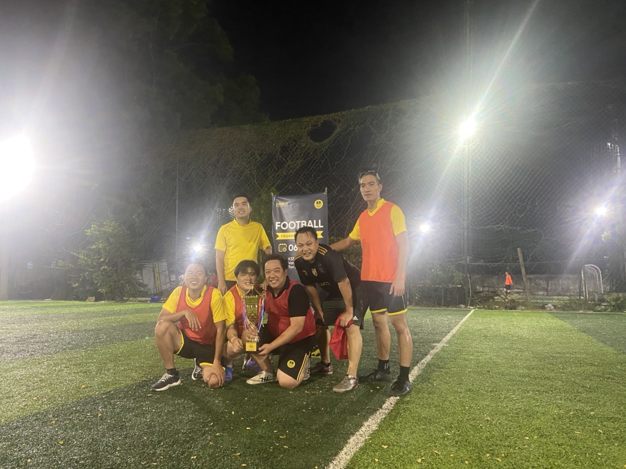 Football tournament winners posing with trophy on illuminated soccer field at night