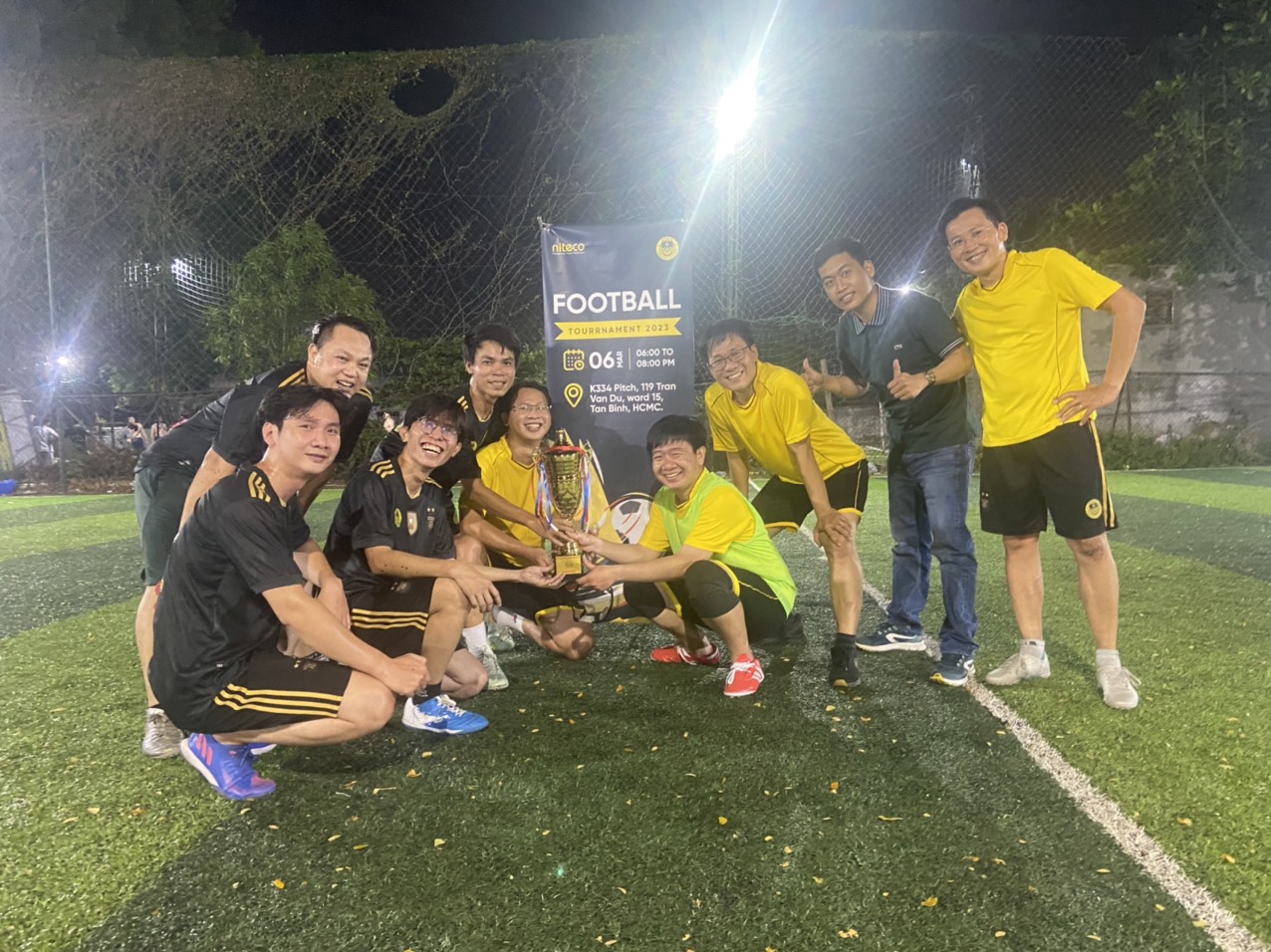 Football tournament 2023 team celebrating victory with trophy on a lit field at night