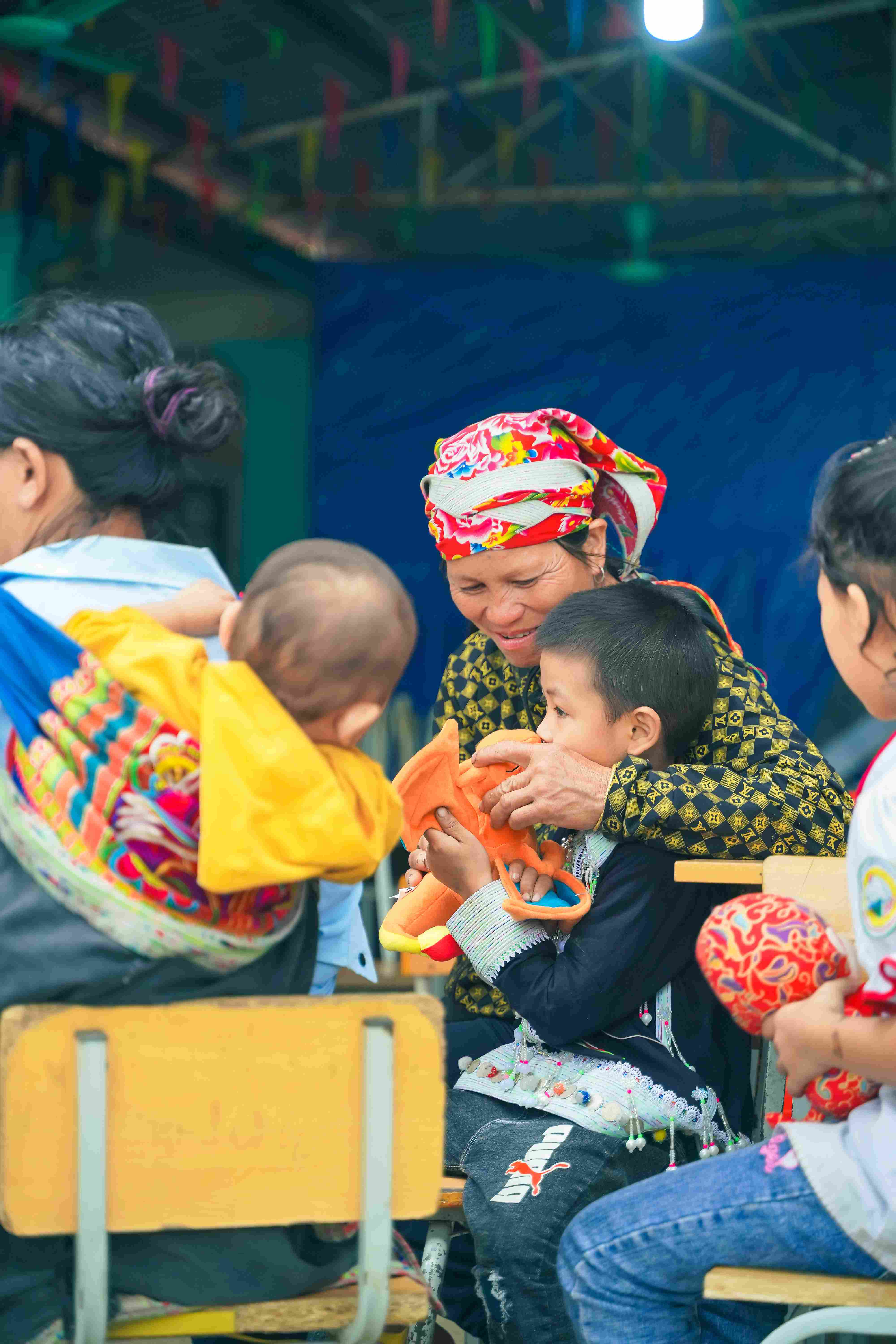 Elder woman and children in traditional attire playing with toys in classroom