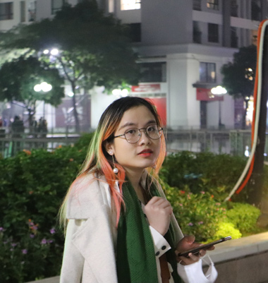 Young woman with pink hair and glasses using smartphone outdoors at night