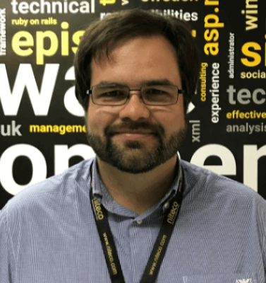 Man with glasses and beard in front of software development keywords background