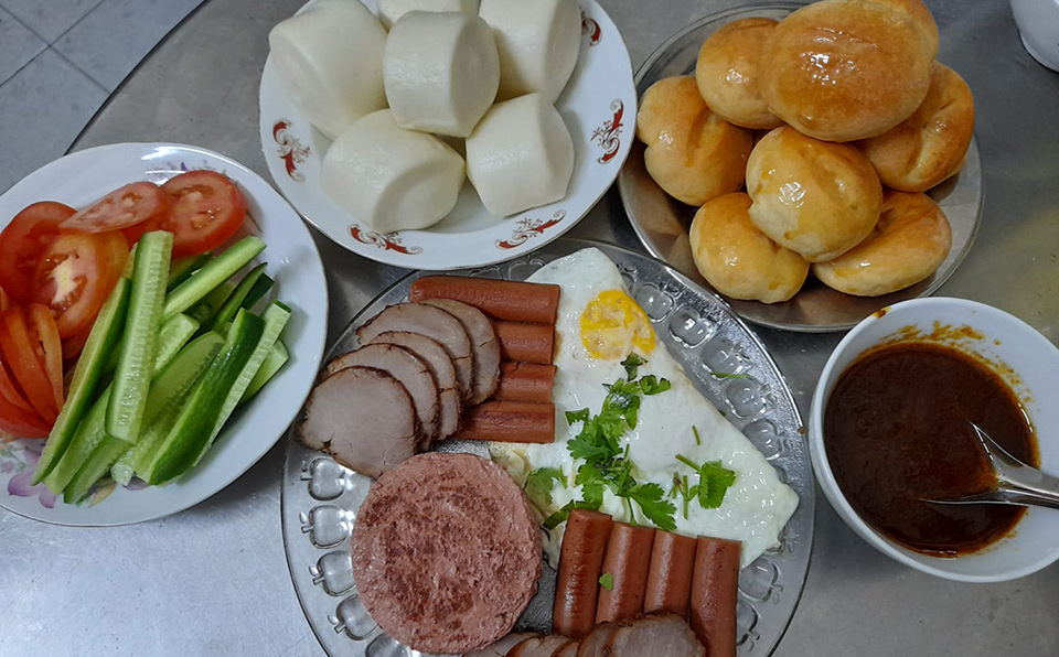 Assorted breakfast platter with steamed buns, bread rolls, eggs, vegetables, and sauce