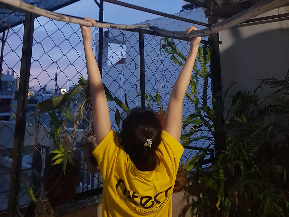 Person doing pull-ups outdoors at dusk with plants and city background
