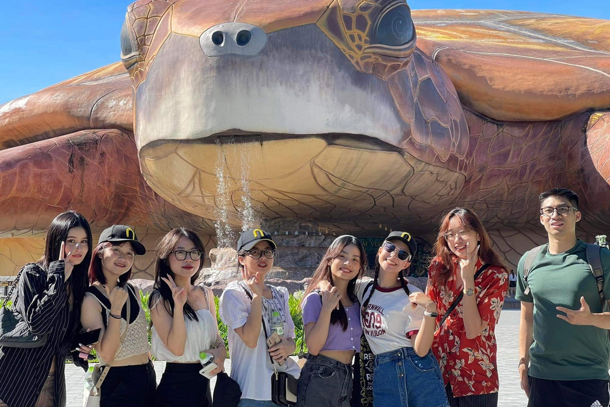 Group of friends posing in front of giant turtle sculpture at tourist spot