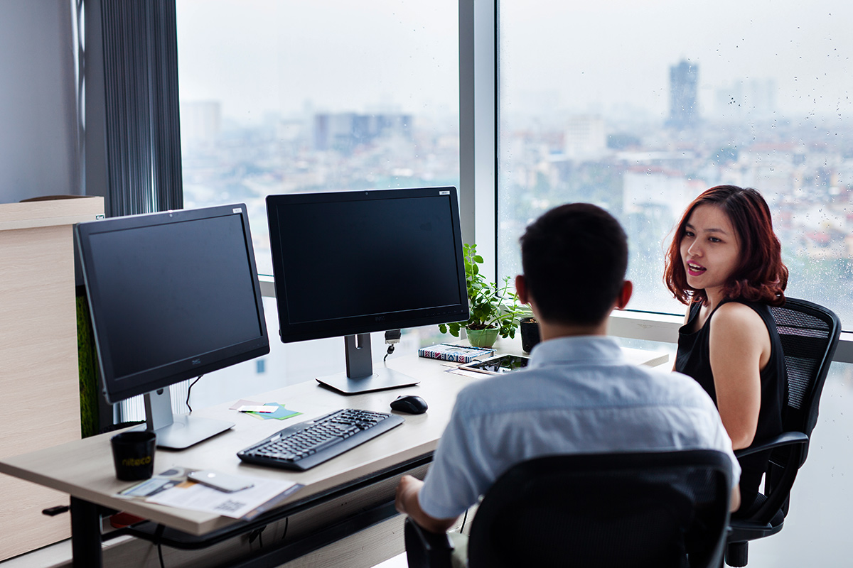 Two coworkers discussing project plans in a modern office with dual monitors