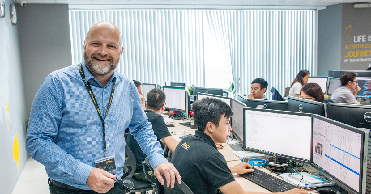 Smiling team leader with software developers working on multiple monitors in office