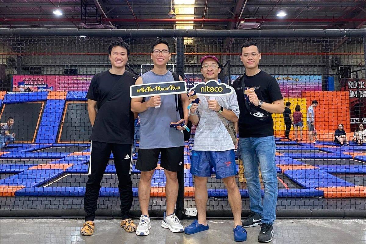 Four men at a trampoline park holding signs with Niteco and #BeTheMoonFlow keywords