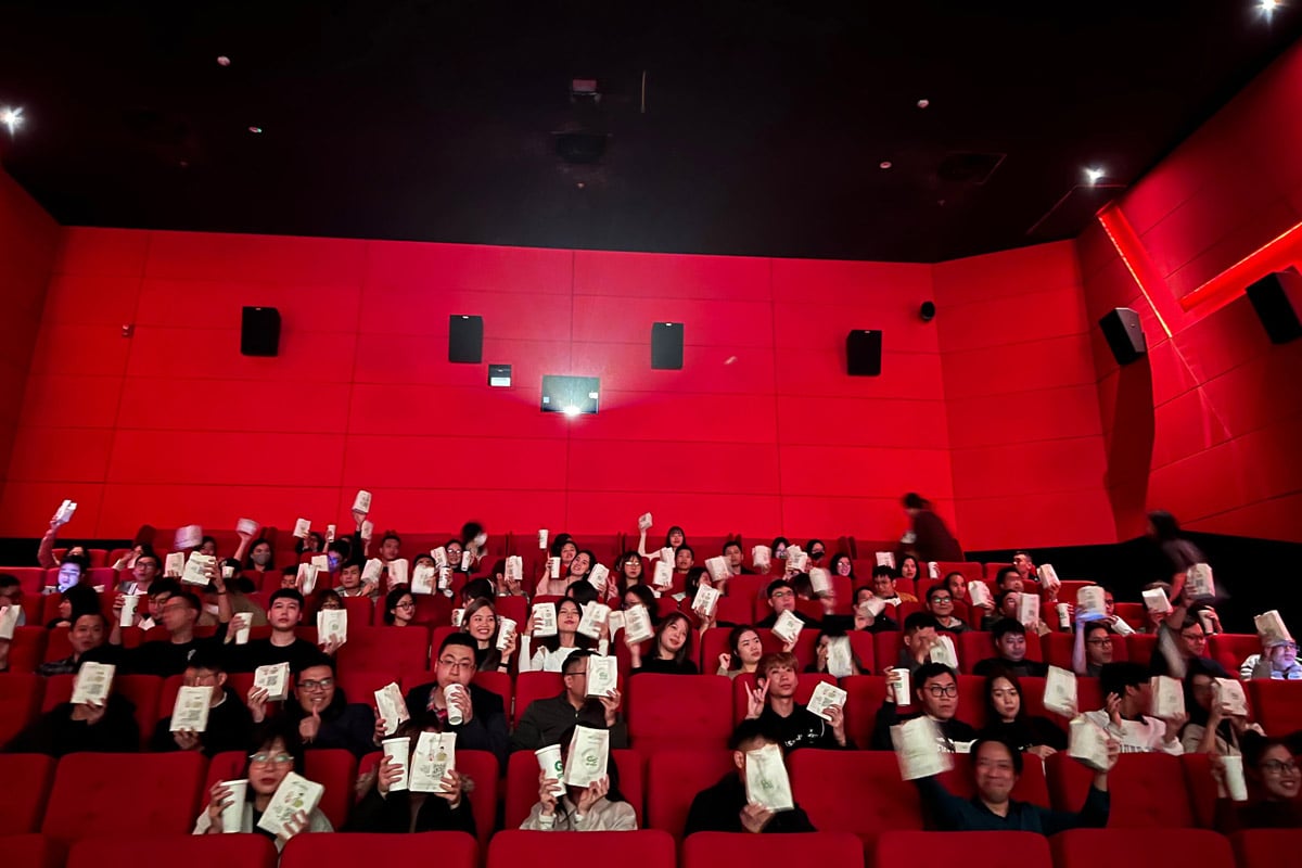 Movie theater audience holding popcorn bags and drinks in red seats