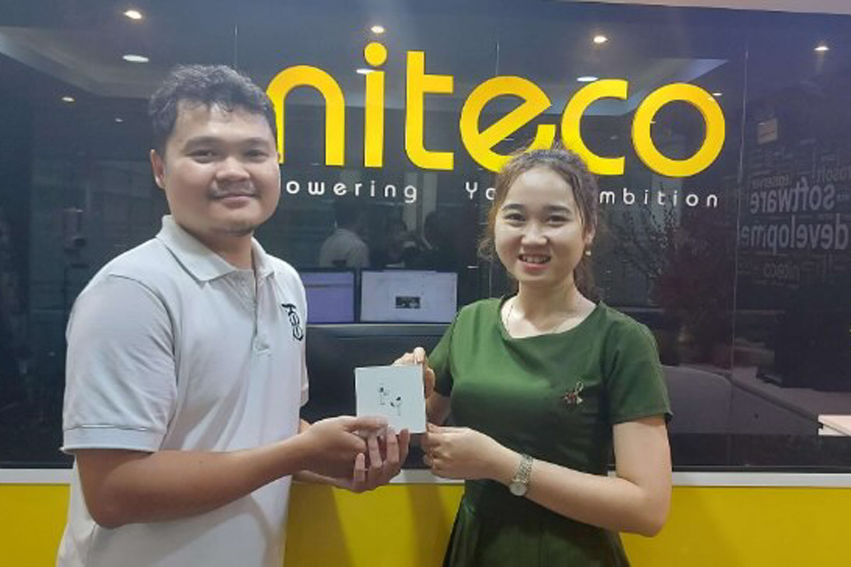 Niteco team members exchanging a tech gadget in office with company logo background