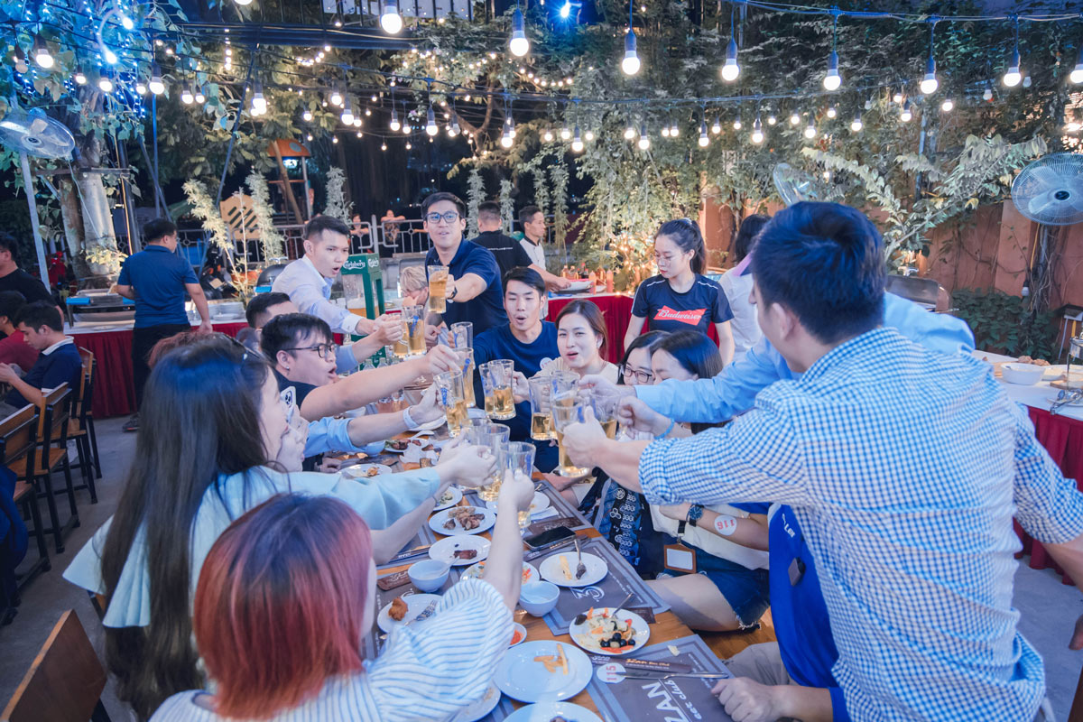 Friends toasting with beer glasses under festive lights at outdoor party