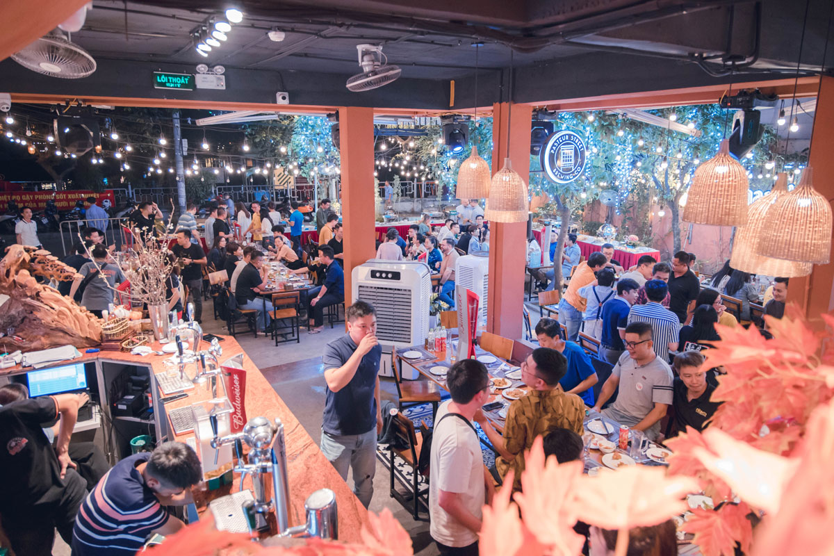 Busy beer garden with groups enjoying food and drinks under string lights