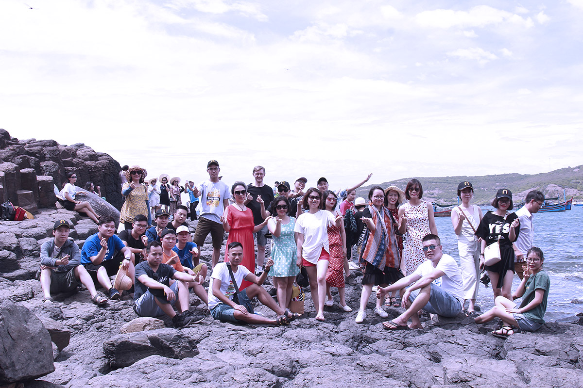Group of tourists posing on rocky shore near the sea during summer trip