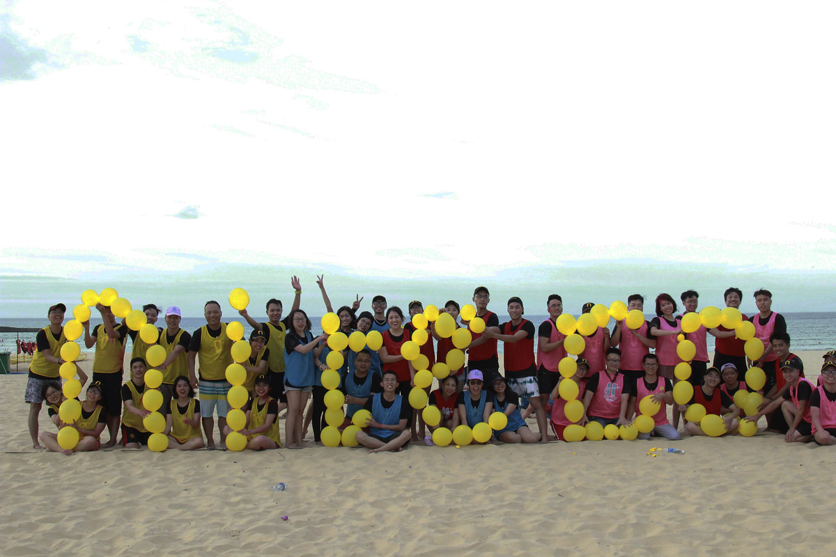 Group holding yellow balloons spelling "QNB 2023" on beach during team event