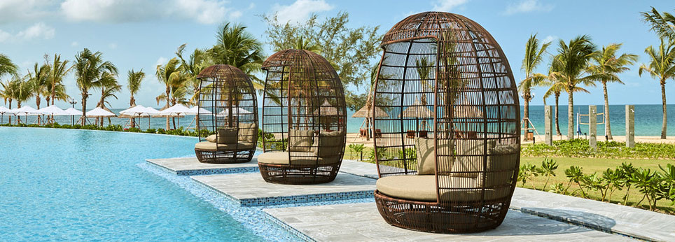 Wicker lounge chairs by the poolside with palm trees and ocean view
