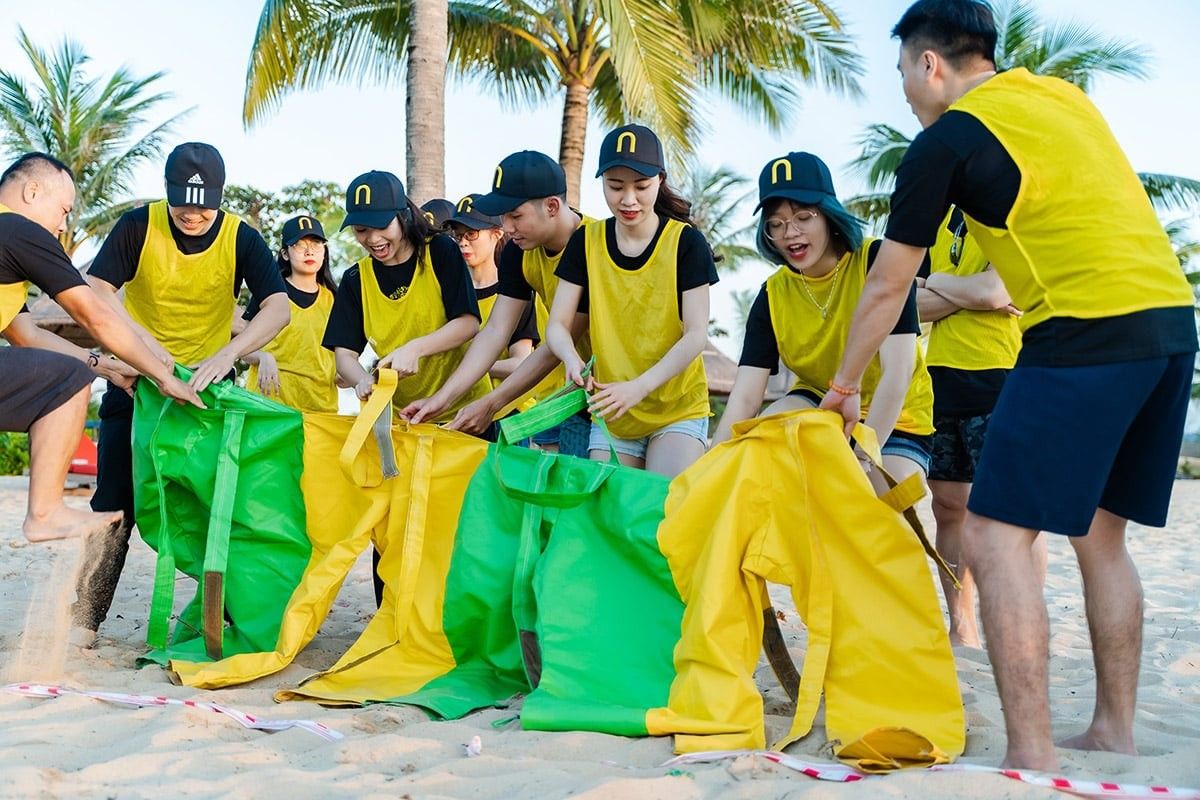 Team-building activity on beach with participants wearing yellow vests and large pants