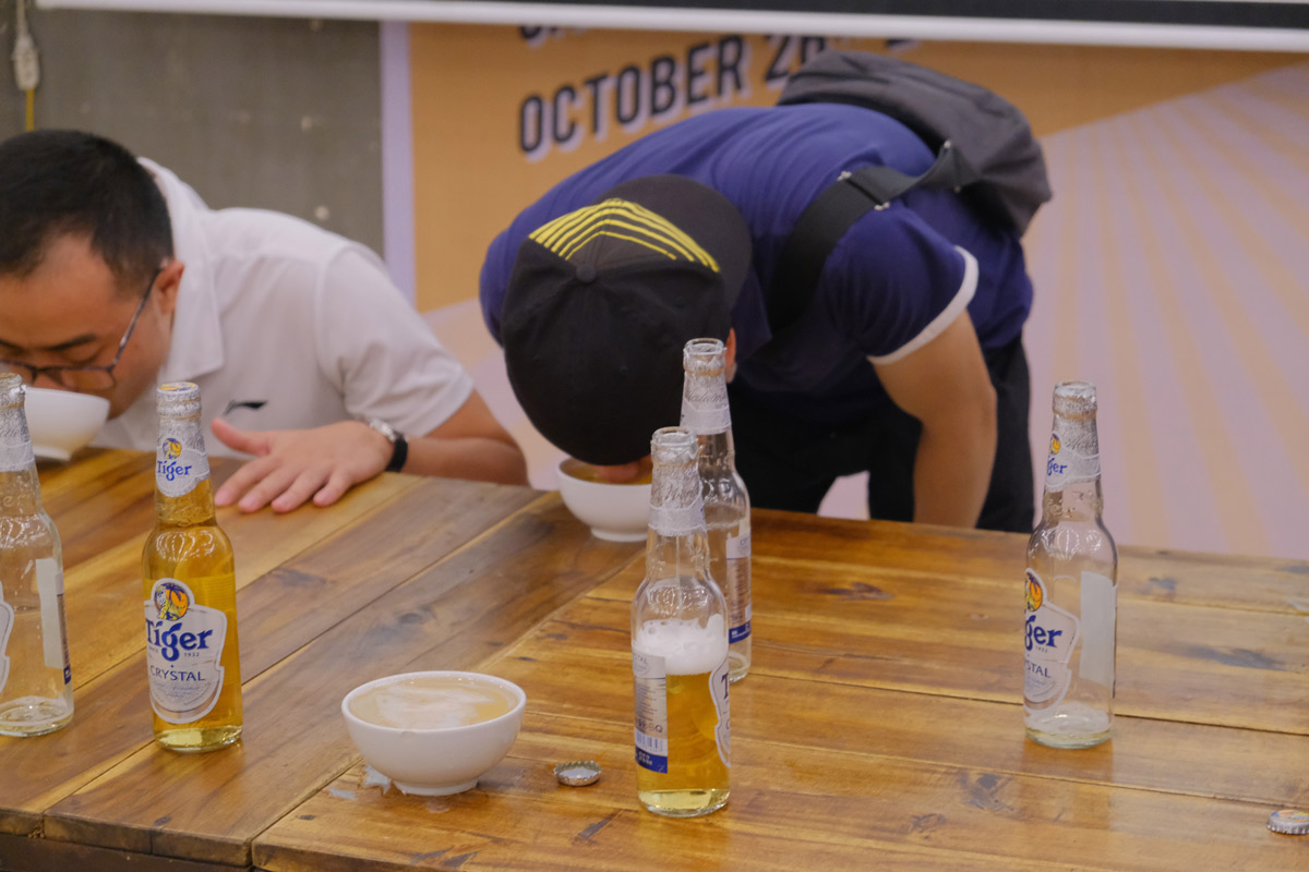 Two men participating in a beer drinking contest with bottles on wooden table