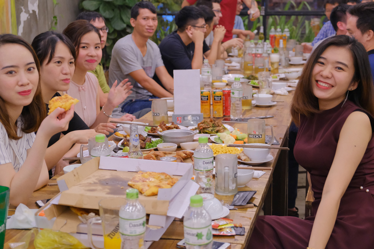 Friends enjoying a group dinner with pizza, drinks, and various dishes on a long table