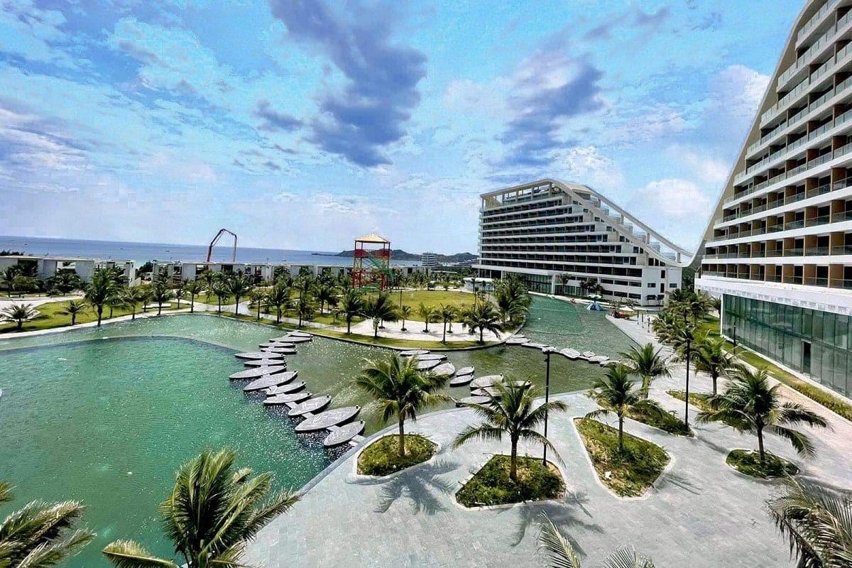 Modern resort with lagoon, palm trees, and ocean under a cloudy blue sky