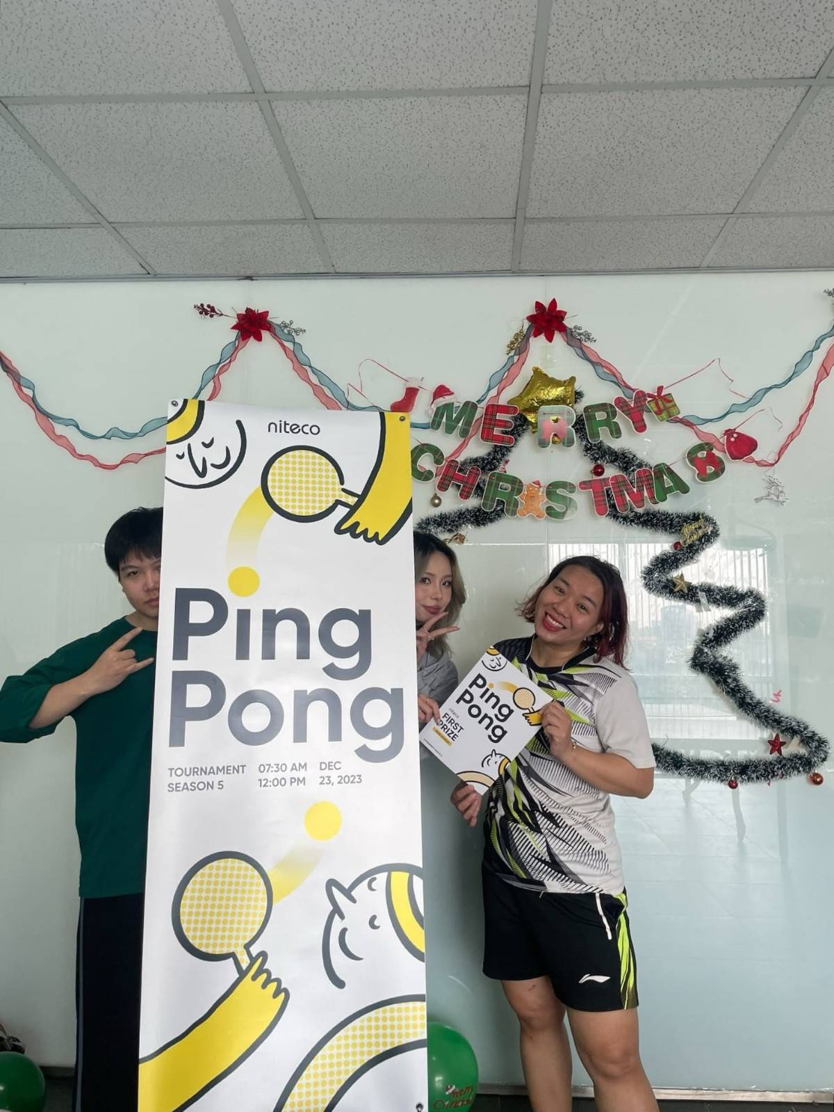 Three people celebrating Ping Pong tournament with Christmas decorations in background