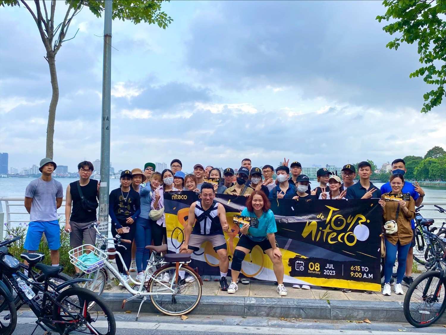 Group of cyclists holding de Tour Niteco banner by the lakeside on July 8, 2023