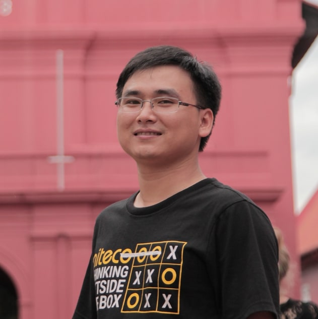 Young man wearing glasses and a shirt with tic tac toe design smiling outdoors