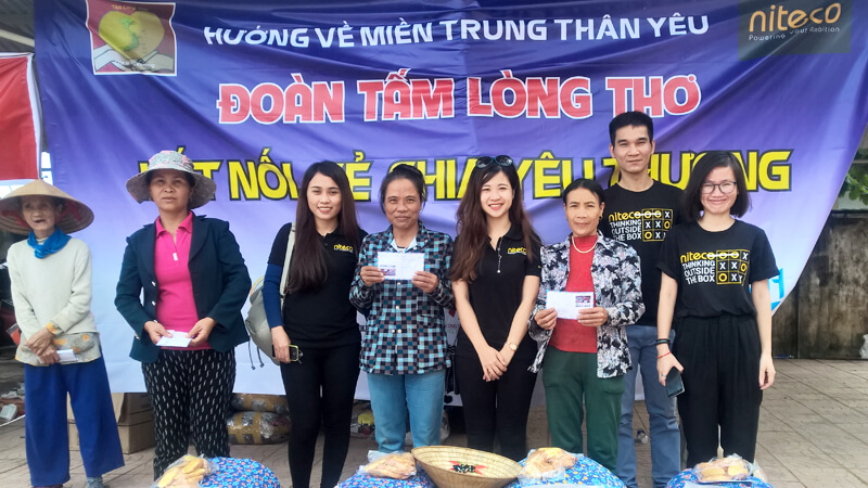 Seven volunteers and locals holding donations at Huong ve Mien Trung charity event banner